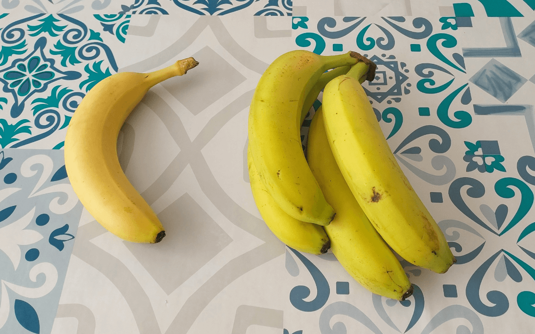 Ripe yellow banana on the left. Bunch of greenish bananas on the right.